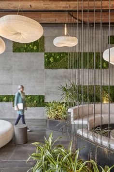 a person walking through a room with plants on the wall and hanging lights above it