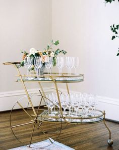 a bar cart filled with wine glasses on top of a wooden floor