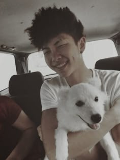 a man holding a white dog in the back of a car