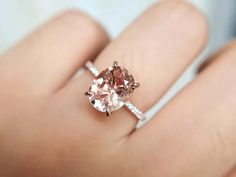 a woman's hand holding an engagement ring with a pink morganite in it