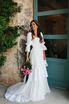 a woman standing in front of a door wearing a white dress and holding a bouquet