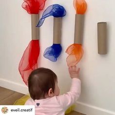 a baby reaching up to some plastic objects on the wall with their hands and fingers