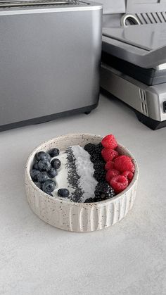 a bowl with berries and blueberries in it next to a toaster on the counter