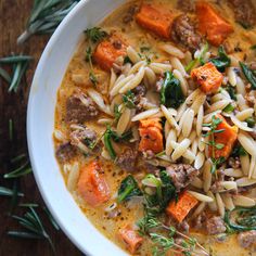 a white bowl filled with pasta, meat and veggies on top of a wooden table