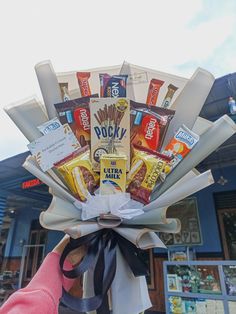 a person holding up a bunch of snacks in front of a building with a sky background