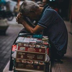 an old man sitting on the curb with his head in his hands