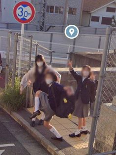 two people with backpacks are walking down the sidewalk near a fence and street signs