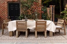 an outdoor table with four chairs and a white tablecloth on it in front of a brick building