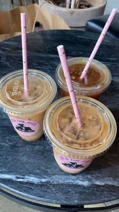 three plastic cups filled with liquid on top of a black marble table and two pink straws sticking out of them