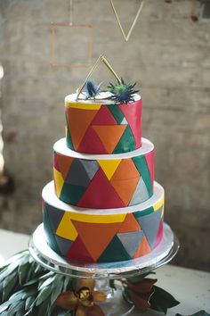 a multi - tiered cake decorated with geometric shapes and greenery sits on a table