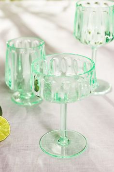 three green glass cups and two lemons on a white table cloth next to each other