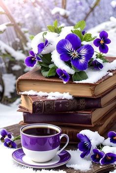 purple flowers are sitting on top of two books and a cup of coffee in the snow