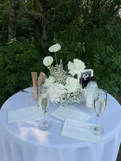 a table topped with two wine glasses filled with white flowers and papers next to each other