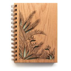 a wooden notebook with an intricate design on the front and back cover, surrounded by palm leaves