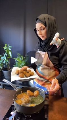 a woman in hijab is cooking food on the stove with a frying pan