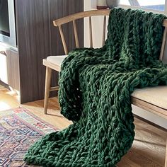 a green knitted blanket sitting on top of a wooden chair next to a window