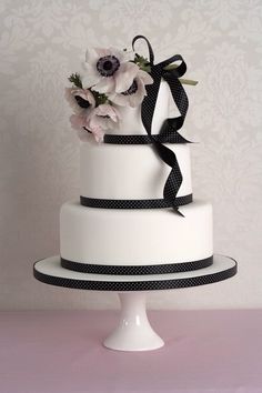 a white wedding cake with black ribbon and flowers