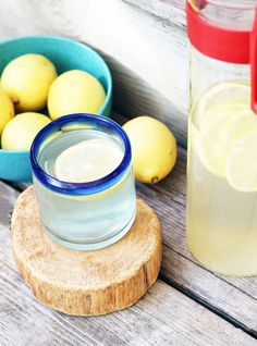 lemons and water are sitting on a wooden table next to two bowls with lemons in them