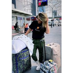 a woman is standing next to her luggage at the airport and talking on her cell phone