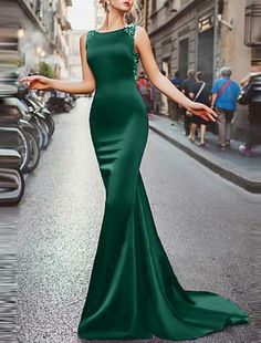 a woman in a long green dress is standing on the street with her arms out