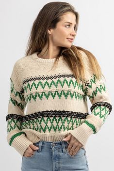 a woman is wearing a sweater with green and white designs on the front, she has her hands in her pockets