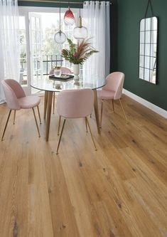 a dining room with green walls and wooden floors, pink chairs around a glass table