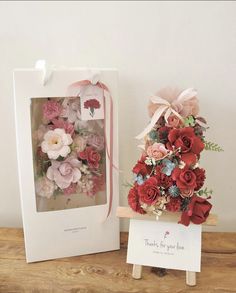 two boxes with flowers in them sitting on a wooden table next to a card holder