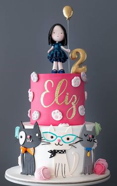 a two tiered cake decorated with cats and a girl holding a balloon on top