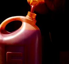 a person is pouring orange liquid into a pink plastic jug with a yellow cap on it