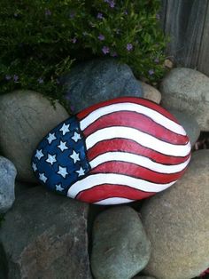 a rock with an american flag painted on it is sitting in the middle of some rocks