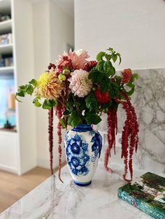 a blue and white vase filled with flowers on top of a marble counter next to a book