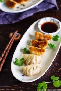 two white plates filled with dumplings next to chopsticks on a wooden table