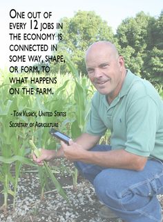 a man kneeling down next to a corn field holding a cell phone in his hand