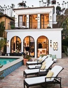 an outdoor patio with lounge chairs and a swimming pool in front of a large house