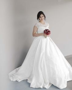 a woman in a white wedding dress holding a red bouquet and posing for the camera