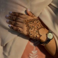 a woman's hand with henna tattoos on her left arm and wrist, holding a watch