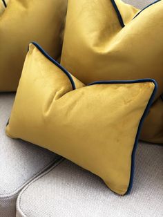 two yellow and blue pillows sitting on top of a white couch next to each other