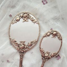 two antique mirrors sitting on top of a white cloth covered table next to each other