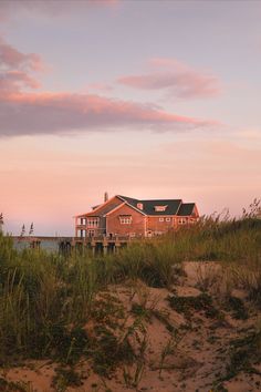 a house sitting on top of a sandy beach next to the ocean under a pink sky