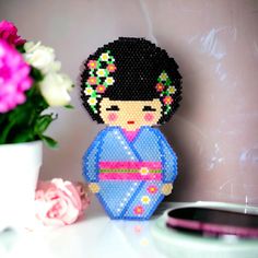 a beaded doll sitting on top of a table next to a vase with flowers