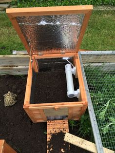 an open wooden box filled with dirt next to a small green planter in the ground