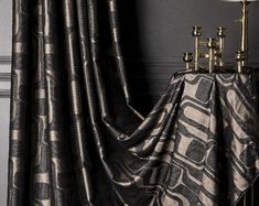 a black and white patterned curtain next to a table with a lamp on top of it