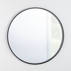 a round mirror hanging on the side of a white wall next to a door and window