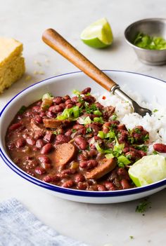 a white bowl filled with beans and rice next to a slice of bread on top of a table