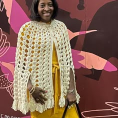 a woman standing in front of a wall with a crocheted shawl on it