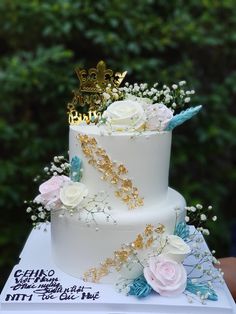 a three tiered white cake with flowers and a gold crown on top sits atop a book