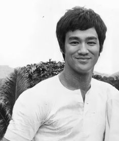 black and white photograph of a young man in front of some bushes smiling at the camera