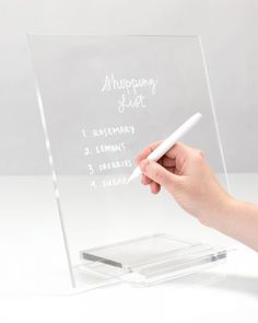 a person writing on a clear acrylic sign with a white pen in their hand