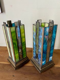 two stained glass vases sitting on top of a wooden table