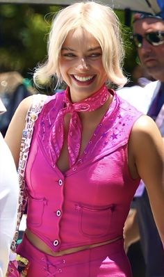 a woman with blonde hair wearing a pink outfit and smiling at the camera while standing next to other people